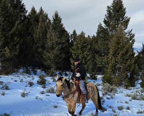 Hunter riding a horse through snowy Wyoming backcountry near Dubois while preparing for a Western hunt.