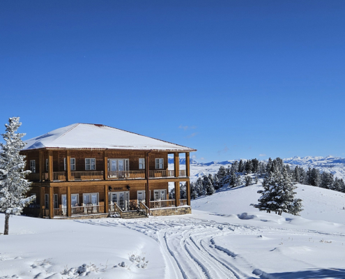 Winter view of Arcady Ridge Ranch cabin in Dubois, Wyoming, surrounded by snow-covered hills with mountain views, offering a peaceful Western ranch retreat.