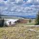 Panoramic view of a Wyoming mountain valley with snow patches, evergreen trees, and distant snow-capped peaks